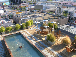 An elevated view of a rooftop terrace featuring a rectangular pool, potted plants, and outdoor dining sets.