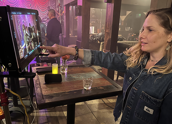 A woman in a denim jacket points at a video monitor displaying a scene being filmed.