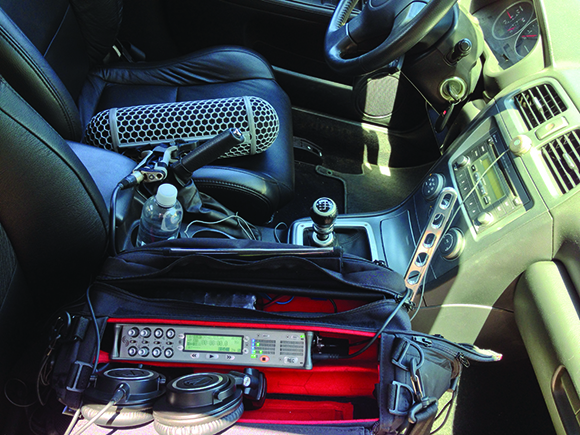 A black bag containing a radio and headphones sits on a car seat next to a water bottle.