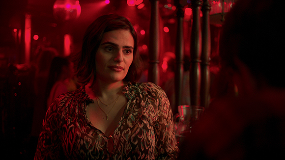 A woman with short dark hair looks sideways in a room bathed in deep red light.