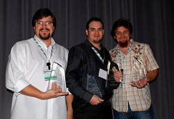 Three men smiling and holding glass awards against a dark curtain.