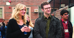 A blonde woman in black and a man with glasses in a dark jacket stand outdoors near a brick building.