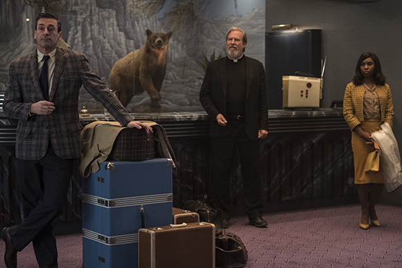 A man in a plaid blazer, a priest in black, and a woman in a yellow skirt stand in a room.