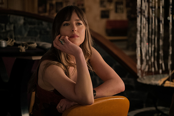 A woman with long brown hair and bangs rests her chin on her hand, looking pensively off-camera.