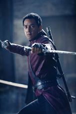 A man in a maroon tunic holds two swords in a combat stance.