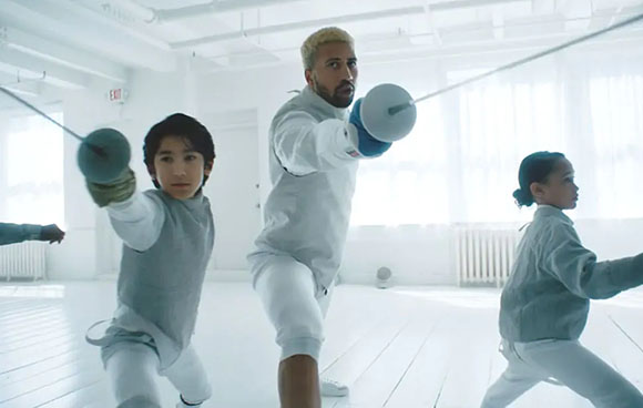 A man and two children in fencing gear lunging with foils in a bright, white studio.
