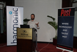 A man stands behind a Hilton podium between Harmonic and Post Magazine banners.