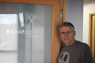 A man in a dark t-shirt stands beside a frosted glass door labeled BARABOOM/ studios.
