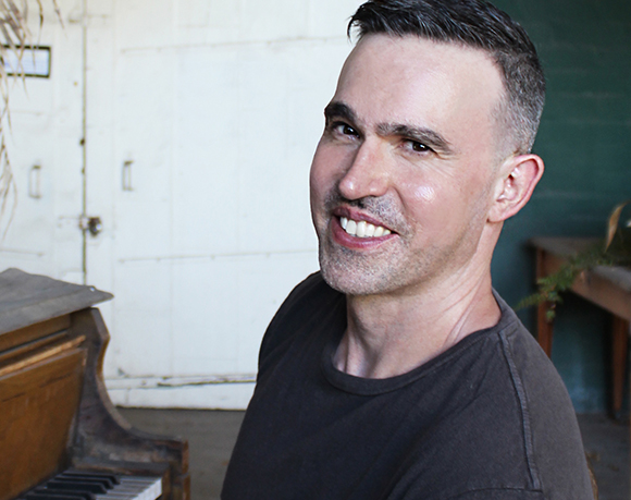 A man with short dark hair smiling towards the camera against a light background.