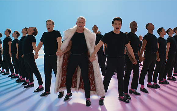 A group of men in black shirts and pants stand in a line on a pink stage, with one man in a white fur coat.
