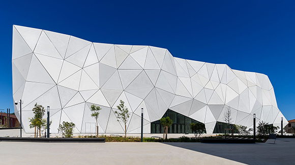 A modern white building featuring a complex, triangular geometric facade against a bright blue sky.