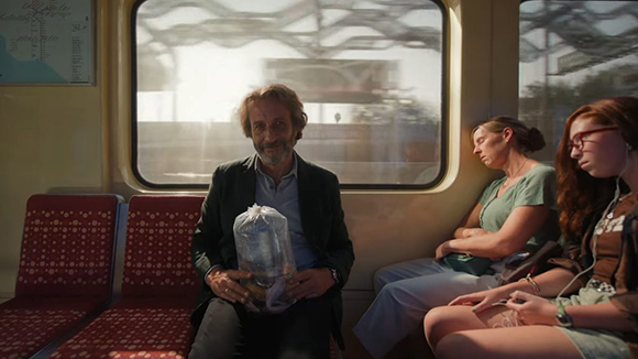 A man sits on a train seat holding a bag, while two women sit beside him.