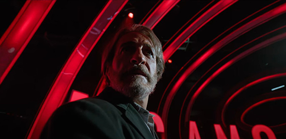 Low angle shot of a bearded man looking up against a background of glowing red curved neon lights.