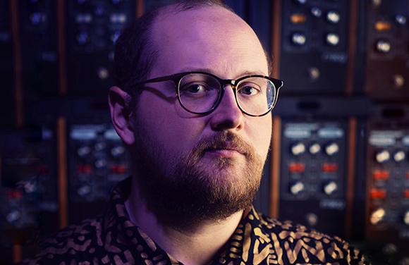A man with glasses and a beard looking at the camera in front of studio equipment.
