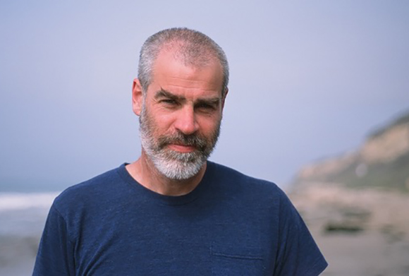 A middle-aged man with short grey hair and a salt-and-pepper beard wearing a blue t-shirt.