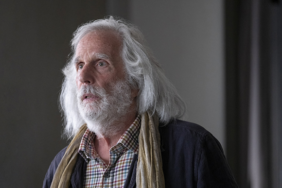 An older man with long, wavy white hair and a full white beard looking to the side.
