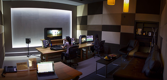 Two people working at computer workstations in a darkened professional video editing studio.