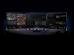 Three computer monitors displaying video editing software above a large control panel with knobs and sliders.