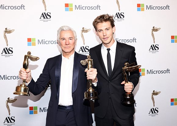 Two men in suits holding gold trophies against a white backdrop with Microsoft and AIS logos.
