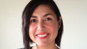 A smiling woman with short dark hair looking toward the camera against a plain light background.