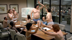 A group of people wearing only underwear sit and stand around a long wooden conference table.