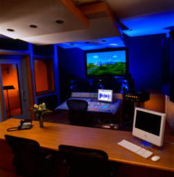 A music production studio with blue lighting, a large screen displaying landscape art, and mixing equipment.