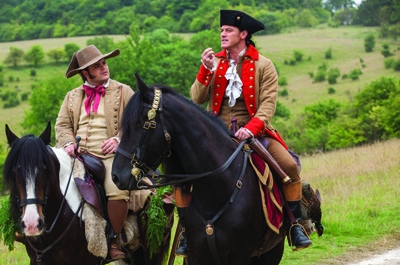 Two men in 18th-century military uniforms riding horses through a green field.