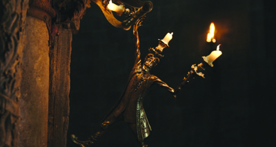 A golden, anthropomorphic candelabra figure with outstretched arms holding lit white candles against a dark background.