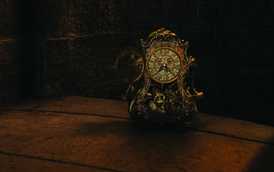 An ornate, antique golden clock with a sun face on the dial sits on a dark wooden surface.