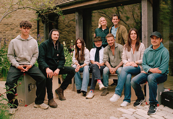 Nine people sit together on a bench and crates in a garden setting.