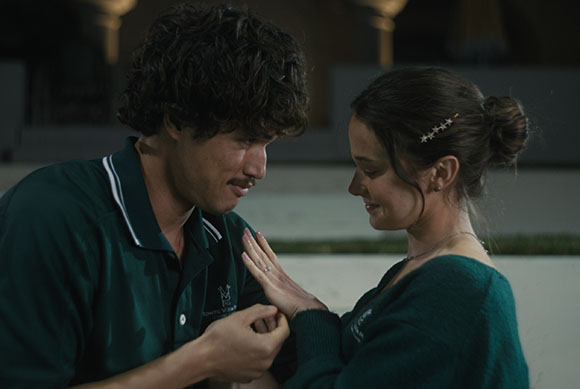 A man in a green polo shirt holds a woman's hand as they gaze at each other outdoors at night.