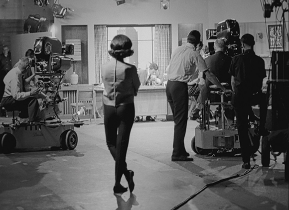 Black and white photo of a film crew operating cameras and equipment on a studio set.