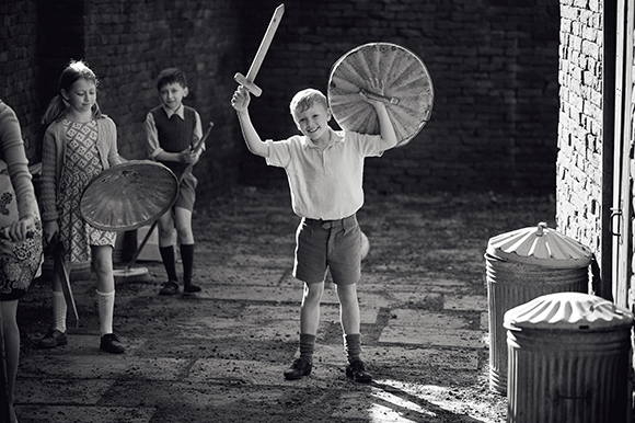 Three children play with toy swords and shields in a brick courtyard.