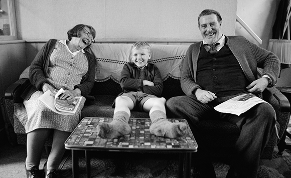 A smiling man, woman, and young boy sitting on a sofa in a living room.