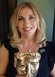 A blonde woman smiling and holding a gold theatrical mask trophy.