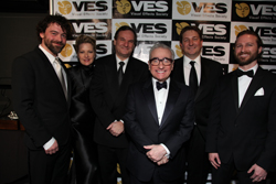 Six people in formal attire posing together in front of a Visual Effects Society backdrop.