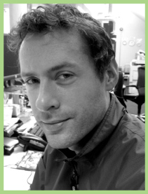 Black and white close-up portrait of a man looking toward the camera in an office.