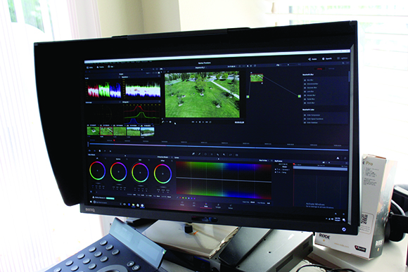 A wide computer monitor showing a video editing interface with timelines, color wheels, and video clips.
