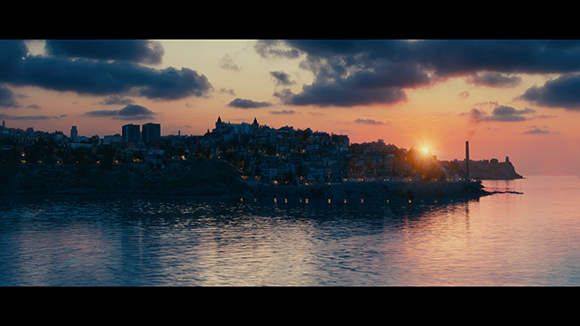 A silhouette of a coastal city on a hill overlooking the ocean during a colorful sunset.
