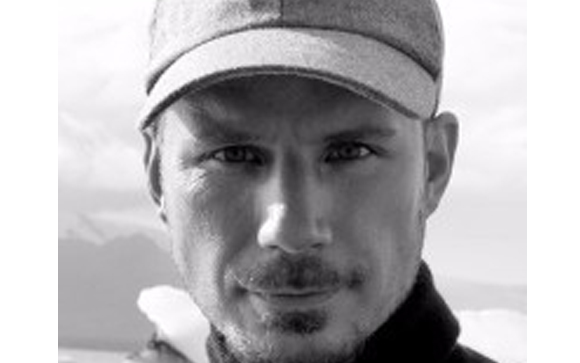 Black and white close-up portrait of a man wearing a flat cap and looking directly at the camera.