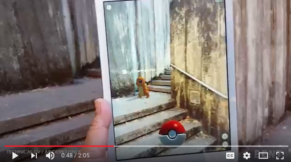 A hand holds a tablet displaying a digital creature on concrete stairs with a Pokéball in the foreground.
