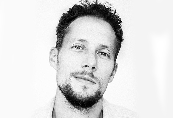 Black and white close-up portrait of a man with curly hair and a goatee looking toward the camera.