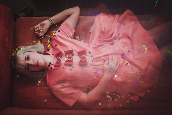A person in a pink dress with bow details lies on a red sofa amidst scattered colorful confetti.