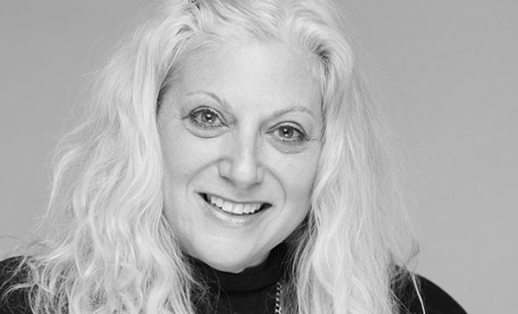 Black and white close-up portrait of a smiling woman with long, wavy, light-colored hair.