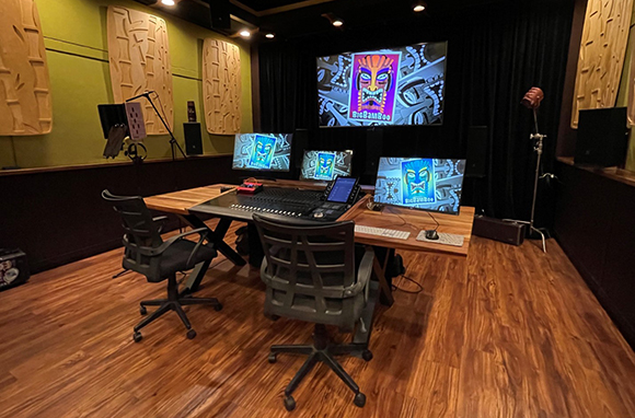 A production studio featuring a large mixing console, multiple computer monitors, and two ergonomic office chairs.