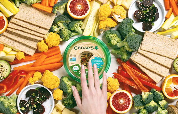 A top-down view of a spread featuring hummus, crackers, carrots, broccoli, cauliflower, and sliced citrus.