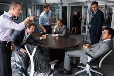 Several business people in formal attire arguing intensely around a dark oval conference table.