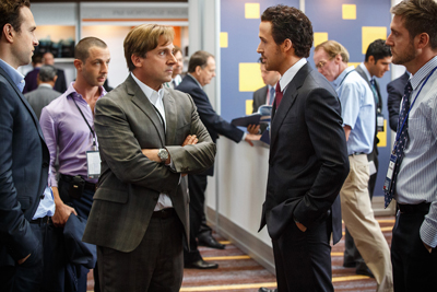 Several men in suits and dress shirts stand in a modern office hallway, engaged in conversation.