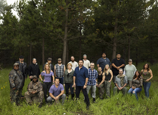 A diverse group of people standing and sitting in a grassy forest clearing.
