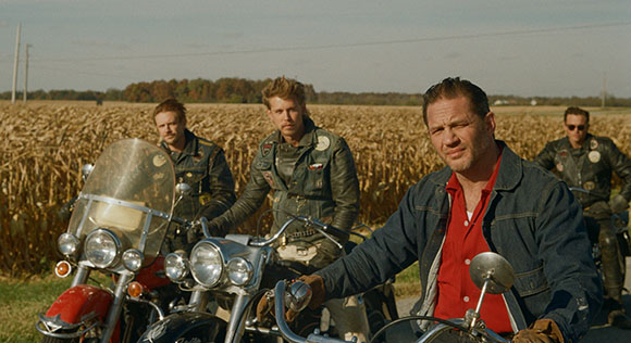 Four men posing with motorcycles in a large cornfield under a clear sky.